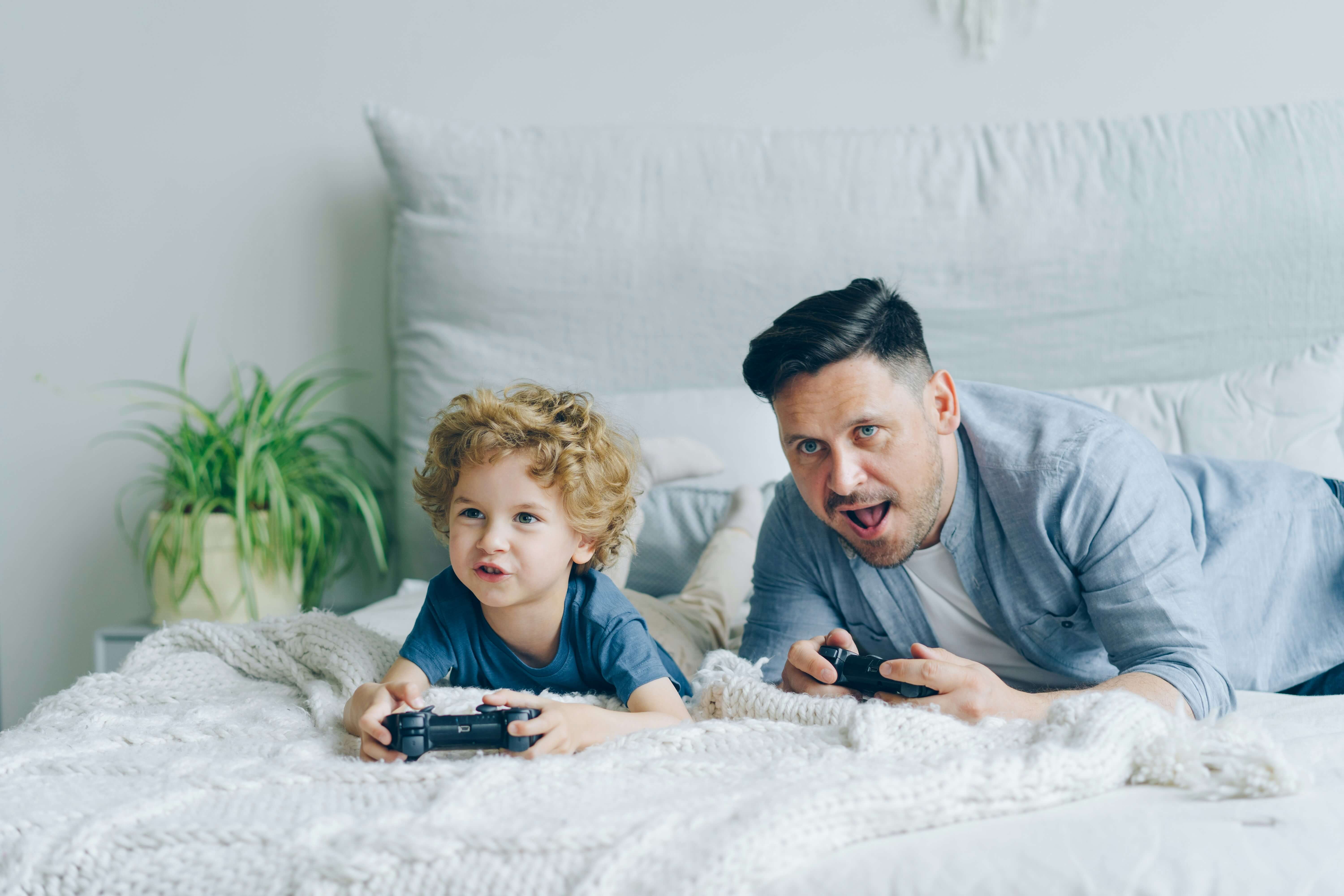 Padre e bambino che tengono in mano dei gamepad sul letto